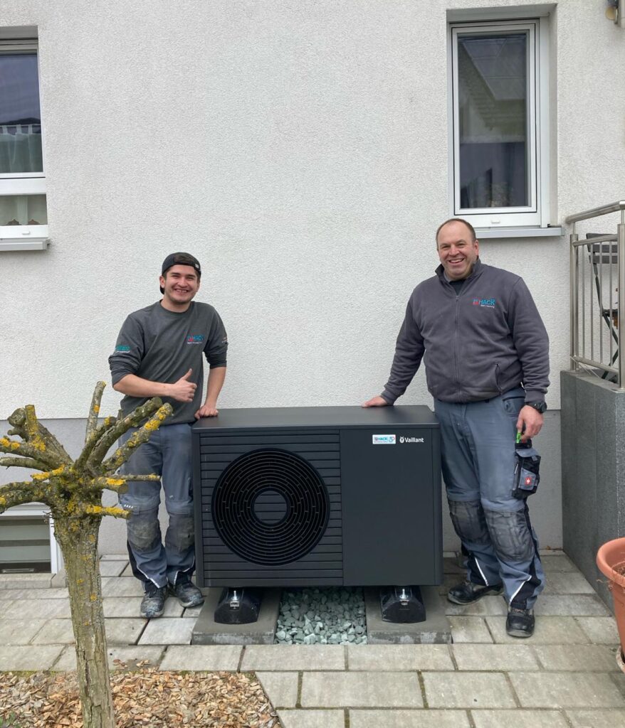 Zwei Männer neben einer installierten Wärmepumpe im Freien.