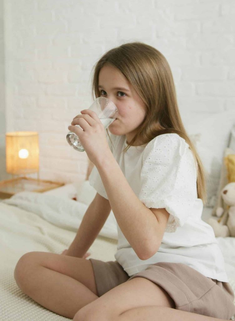 Mädchen sitzt auf Bett und trinkt Milch